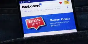 Een smartphone met de bol.com-website open, waarop een 'Bulk alert' advertentie te zien is, steekt uit de zak van een jeans.