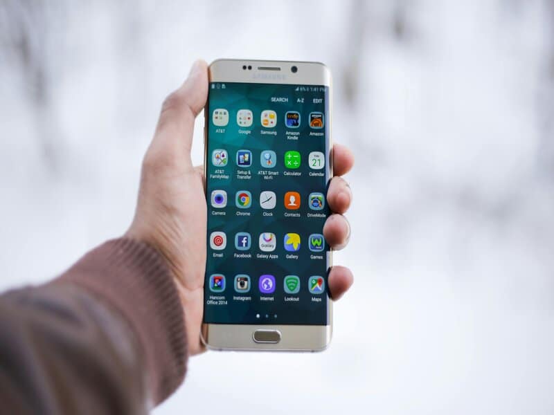 Een hand houdt een smartphone met een scherm vol apps; een scenario waarbij men wellicht de 'Zoekgeschiedenis Verwijderen' wil voor meer privacy en overzicht.